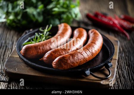 Saucisses fumées de porc au poivre avec du romarin dans une poêle en fonte. Banque D'Images