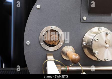 Torréfacteur de café industriel photo en gros plan, les graines de café à torréfier tournent à l'intérieur derrière une petite fenêtre technologique ronde Banque D'Images