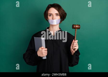 Photo de grave belle femme attrayante avocat de juge ferme la bouche tenant le gavel isolé sur fond de couleur verte Banque D'Images