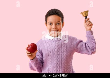 Petit écolier afro-américain avec cloche et pomme sur fond rose Banque D'Images