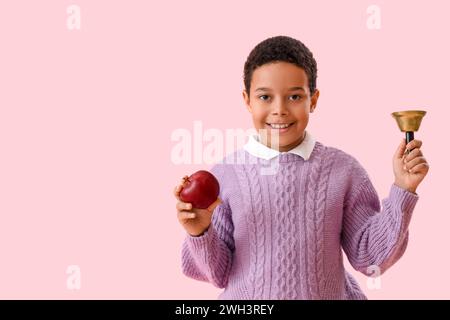 Petit écolier afro-américain avec cloche et pomme sur fond rose Banque D'Images