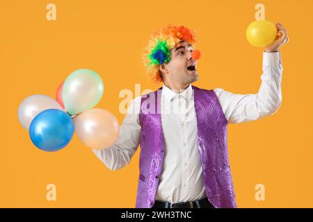 Heureux jeune homme en costume de clown avec des ballons sur fond jaune Banque D'Images