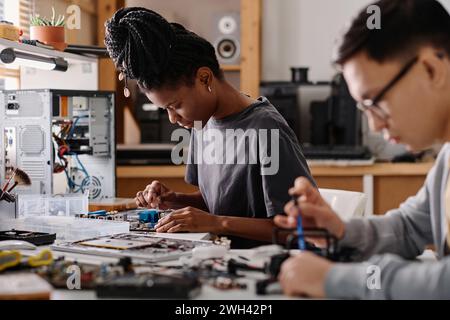 Réparateur féminin noir fixant l'appareil électronique avec un tournevis, son collègue masculin travaillant à proximité Banque D'Images