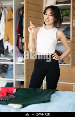 Heureuse jeune fille asiatique essayant de choisir une robe debout par garde-robe Banque D'Images