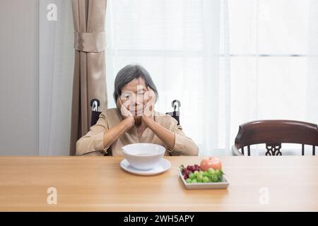 Femme asiatique solitaire âgée s'ennuiant avec de la nourriture. Banque D'Images