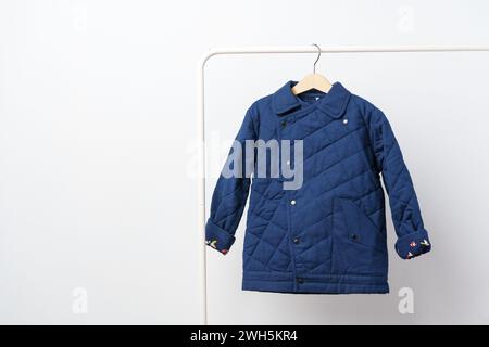 Manteau bleu matelassé pour enfants sur cintre contre mur blanc Banque D'Images