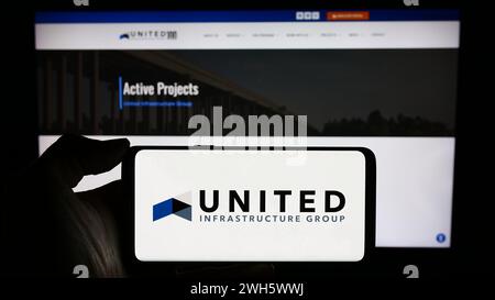 Personne tenant le téléphone portable avec le logo de la société d'investissement américaine United infrastructure Group devant la page Web de l'entreprise. Concentrez-vous sur l'affichage du téléphone. Banque D'Images