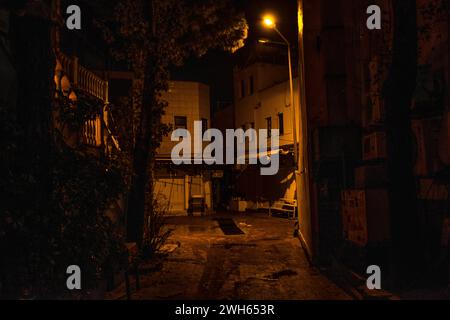 Une vue d'ambiance et d'humeur sombre d'une rue sombre la nuit après la pluie, avec des lumières de la ville brillantes et des reflets humides créant une ambiance urbaine. Banque D'Images