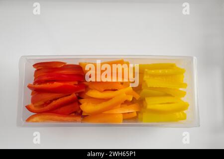 Une vue de dessus de poivrons colorés tranchés Julienne dans un bac en plastique transparent sur un plateau blanc Banque D'Images