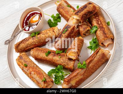 gros plan de jambon et fromage rouleaux de pain grillé français de blé entier servis avec une sauce chili sucrée sur une assiette sur une table en bois blanc Banque D'Images