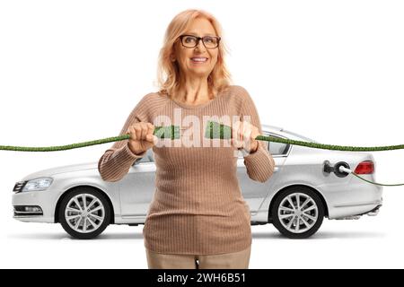 Femme mature heureuse branchant des câbles électriques verts pour une voiture électrique isolée sur fond blanc Banque D'Images