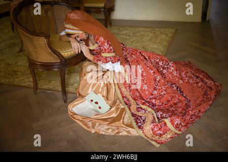 Jeune femme en costume de renaissance médiévale et capot français assis sur le plancher tenant une lettre Banque D'Images