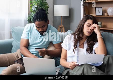 L'accent young couple payer les factures en ligne sur ordinateur portable avec séance documents ensemble sur canapé à la maison, homme et femme confondu sérieux budget planification e Banque D'Images