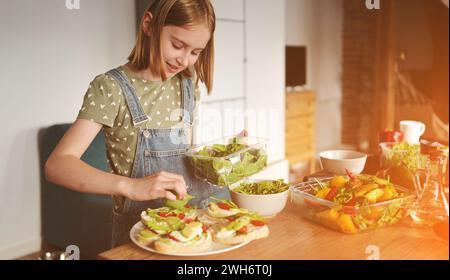 Fille préparant des sandwichs avec avocat, tomates cerises et roquette à la cuisine. Bruschettas végétariennes et salade avec légumes frais et légumes verts Banque D'Images