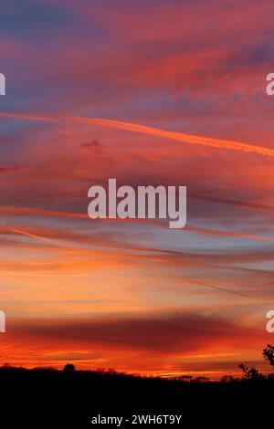 Des traînées de vapeur traversent le ciel captant des rayons de lumière du soir et contrastant avec les nuages multicolores d'un coucher de soleil spectaculaire, le 4 février 2024. Banque D'Images