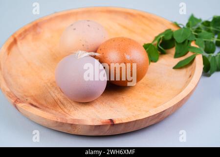 Oeufs de poule entiers dans un plat en bois avec des feuilles vertes sur un fond blanc Banque D'Images