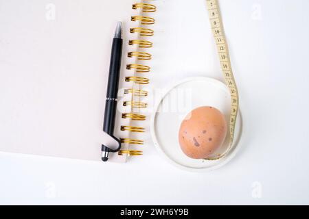 Oeuf de poule et ruban à mesurer et stylo sur fond blanc. Concept de régime Banque D'Images