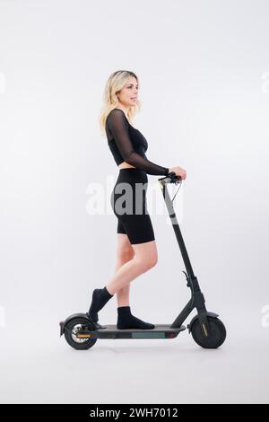 Une femme blonde sur fond rouge assise sur scooter électro et se reposant, copiez l'espace Banque D'Images