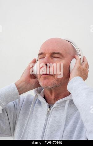 homme chauve mature portant des écouteurs écoutant de la musique avec les yeux fermés. Banque D'Images