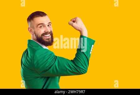 Homme heureux en costume vert sourit, fléchit son bras et montre ses muscles biceps forts Banque D'Images