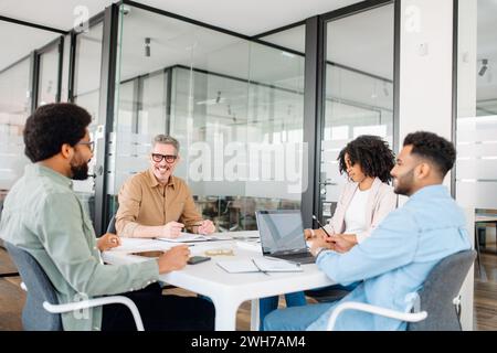 Un groupe diversifié de professionnels est réuni autour d’une table de réunion dans un espace de bureau contemporain, activement engagé dans une séance de brainstorming productive. Banque D'Images