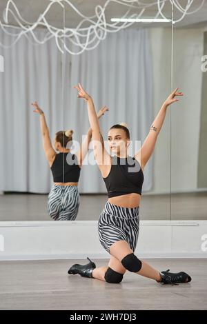 Un danseur gracieux aux talons hauts et une tenue active en noir et blanc, s'équilibre gracieusement sur un genou Banque D'Images