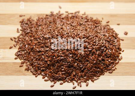 De nombreuses graines brutes de lin reposent sur une planche de cuisine en bois. Ingrédient cru de boulangerie. Vue de dessus. Effectuer la mise au point au centre des grains Banque D'Images