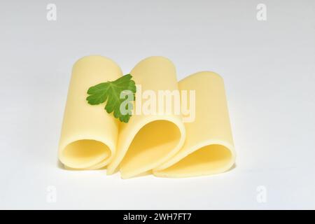 Trois tranches de fromage jaune roulées en tubes reposent sur un fond blanc. Banque D'Images