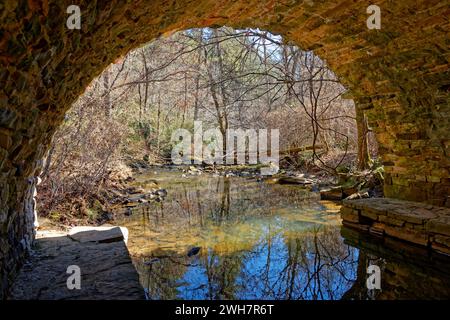 Debout sur un rebord en dessous à l'intérieur de l'arche d'un vieux pont de pierre donnant sur un ruisseau tranquille en hiver par une journée ensoleillée brillante Banque D'Images