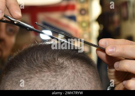 À l'aide de ciseaux et d'un peigne, le coiffeur enlève les cheveux de l'arrière de la tête du client. Banque D'Images