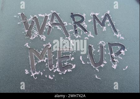 Gros plan du message « Warm me Up » écrit avec un doigt sur le pare-brise d'une voiture givré lors d'un coup de froid dans le West Sussex, Angleterre, décembre 2023. Banque D'Images