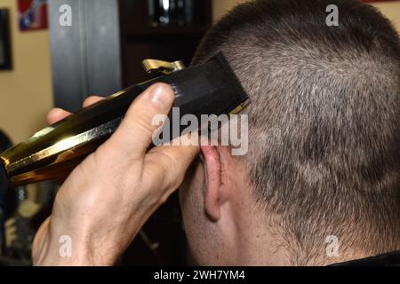 Un coiffeur coupe les cheveux sur le côté de la tête d'un client avec une tondeuse. Banque D'Images