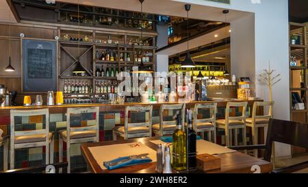 Un restaurant élégant orné de bouteilles de vin et doté de tables en bois rustiques accompagnées d'élégantes chaises blanches Banque D'Images