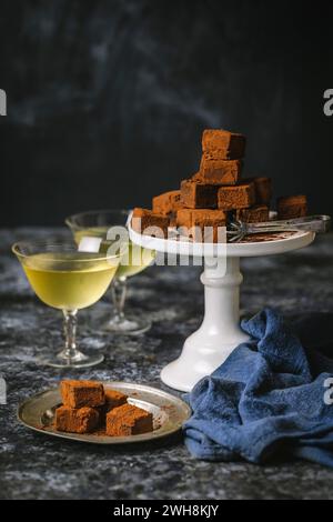 Arrangement de truffes au chocolat saupoudrées de poudre de cacao sur un présentoir à gâteau avec un jeu de pinces en argent, et petite assiette en argent avec 2 verres vintage f Banque D'Images