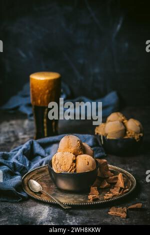 Plan avant d'un bol noir avec 3 boules de crème glacée au chocolat et une pinte mousseuse de bière brune avec des chiffons en lin bleu foncé Banque D'Images