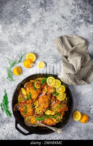 Cuisses de poulet dans une poêle en fonte avec citrons frais et rôtis, fenouil et échalotes sur fond gris avec garniture de citron tranché Banque D'Images