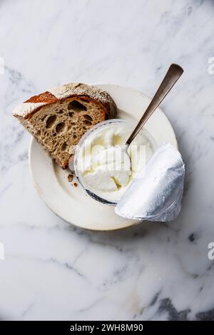 Le lait aigre Clabber dans boîte en plastique avec bouchon aluminium et pain de seigle marron sur fond de marbre blanc Banque D'Images