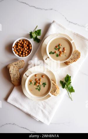 Soupe végétalienne au chou-fleur, cumin et haricots de Lima sur marbre blanc de paillasse servie dans deux bols à soupe, flatlay. Banque D'Images