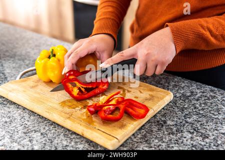 gros plan des mains de la femme coupant des poivrons sur une planche à découper au comptoir de la cuisine Banque D'Images