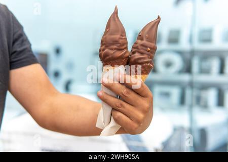 Main d'homme tenant deux glaces à la crème recouvertes de chocolat dans un cône Banque D'Images