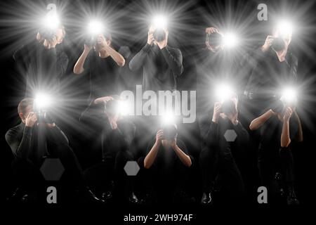Groupe de photographes avec des appareils photo sur fond noir. Paparazzi prenant des photos avec des flashs Banque D'Images