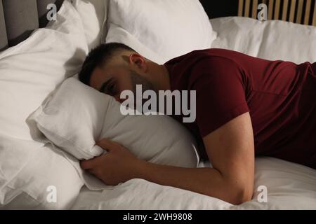 Homme triste cachant le visage dans l'oreiller sur le lit à la maison Banque D'Images