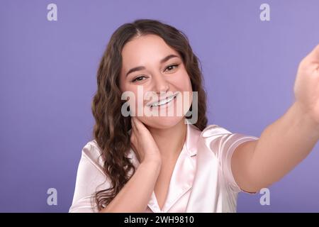 Femme souriante avec des accolades prenant selfie sur fond violet Banque D'Images