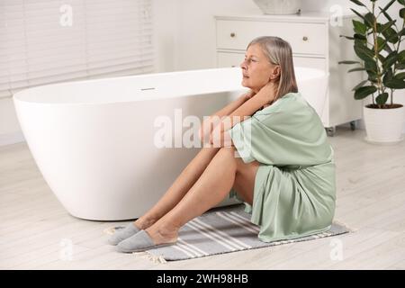 Ménopause. Femme souffrant de douleur dans le cou près de la baignoire dans la salle de bain Banque D'Images