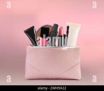 Sac cosmétique rempli de produits de maquillage sur fond rose Banque D'Images