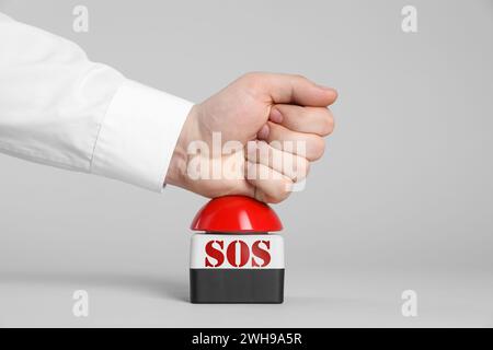 Homme appuyant sur le bouton rouge SOS sur fond blanc, gros plan Banque D'Images