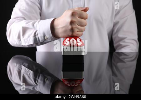 Homme appuyant sur le bouton rouge SOS à la table noire, gros plan Banque D'Images