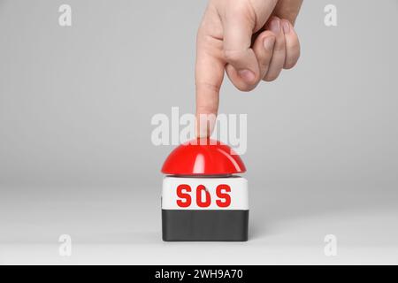 Homme appuyant sur le bouton rouge SOS sur fond blanc, gros plan Banque D'Images