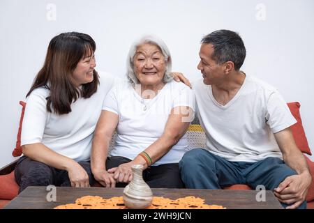Les enfants adultes embrassent chaleureusement leur mère âgée, qui regarde directement la caméra avec un sourire joyeux. Banque D'Images