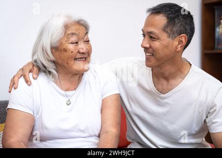 Mère asiatique regardant son fils adulte assis sur un canapé à la maison, concept de style de vie familial heureux. Banque D'Images